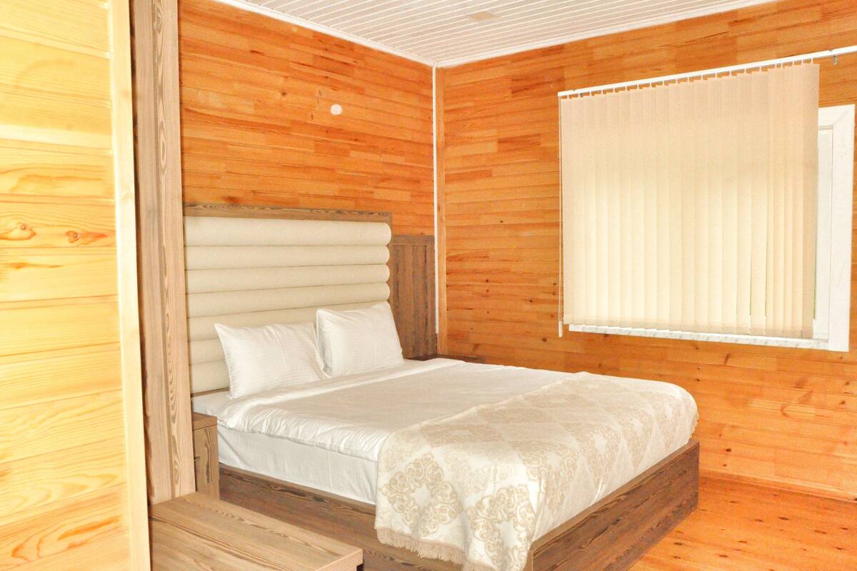 Een kamer met houten lambrisering, een bed, een raam met zonwering en een houten bank.