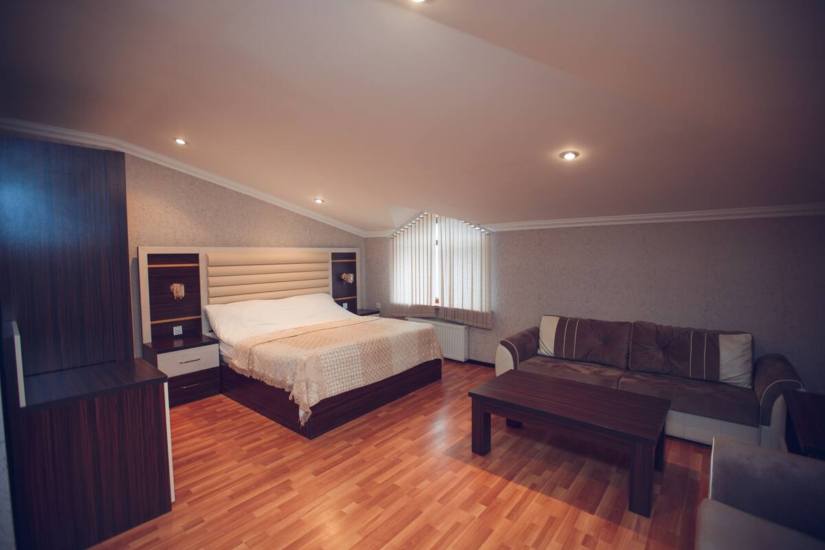 Een slaapkamer met een groot bed, een houten vloer, een bank, een bijzettafeltje en inbouwkasten.