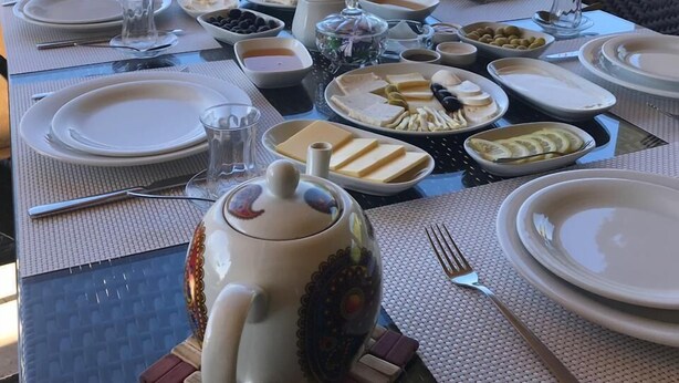 A table set for breakfast with various dishes, a teapot, and a view of a lake and mountains in the background.