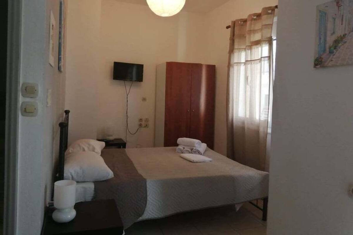 A bedroom with a bed, a television mounted on the wall, a wardrobe, and a window with curtains.