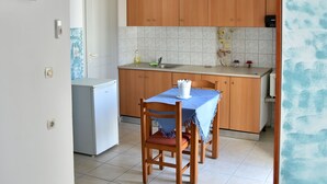 A compact kitchen with wooden cabinets, a small refrigerator, and a dining table set with a blue tablecloth. - Chalkidonos (Heraklion)