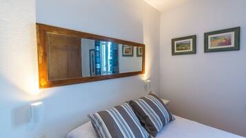 Une chambre avec un grand miroir, un lit agrémenté d’oreillers à rayures et deux tableaux encadrés accrochés au mur.