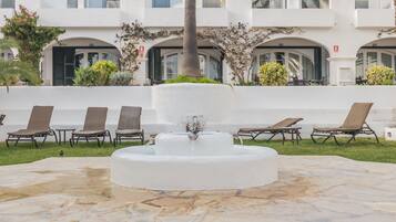 Une cour intérieure avec une fontaine centrale, des chaises longues et un bâtiment blanc doté de balcons.