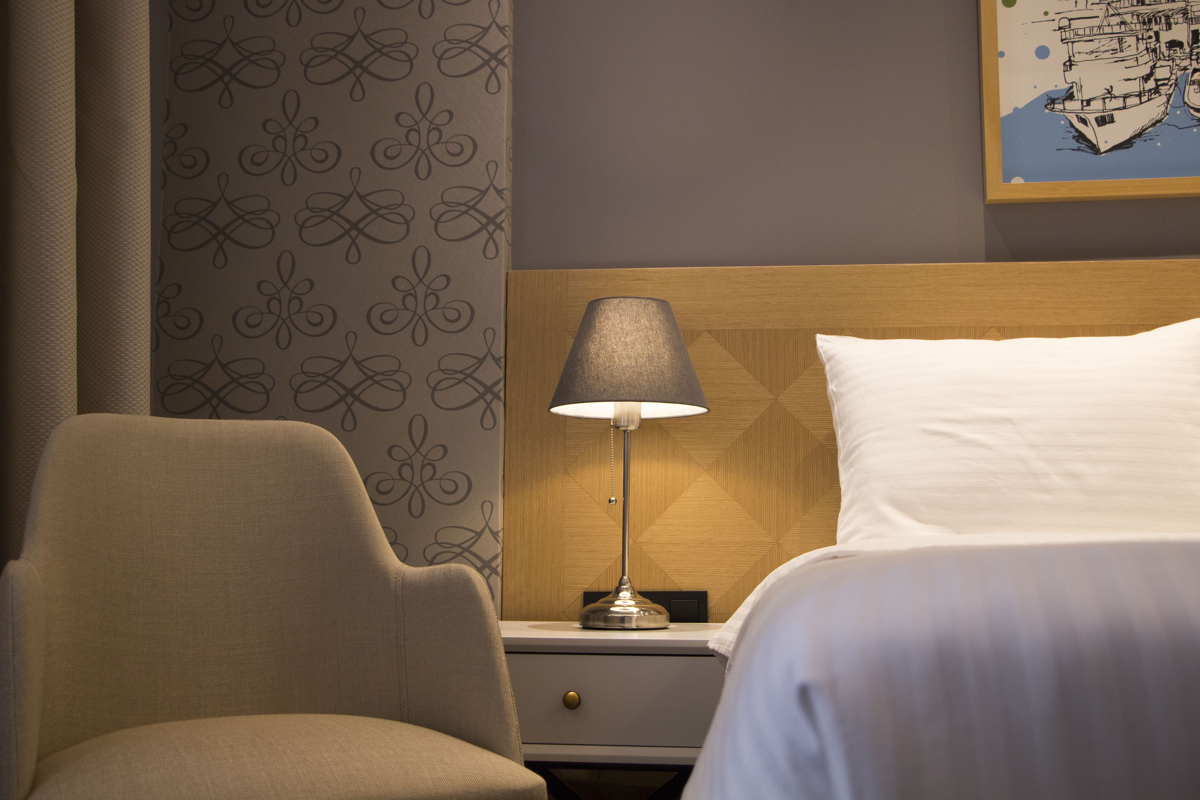 Ein Hotelzimmer mit einem Bett, einem Nachttisch mit Lampe, einem Sessel und einer Wand mit Muster.