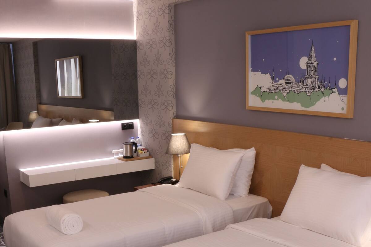 Habitación de hotel con dos camas, un escritorio, un espejo, un cuadro y una alfombra estampada.