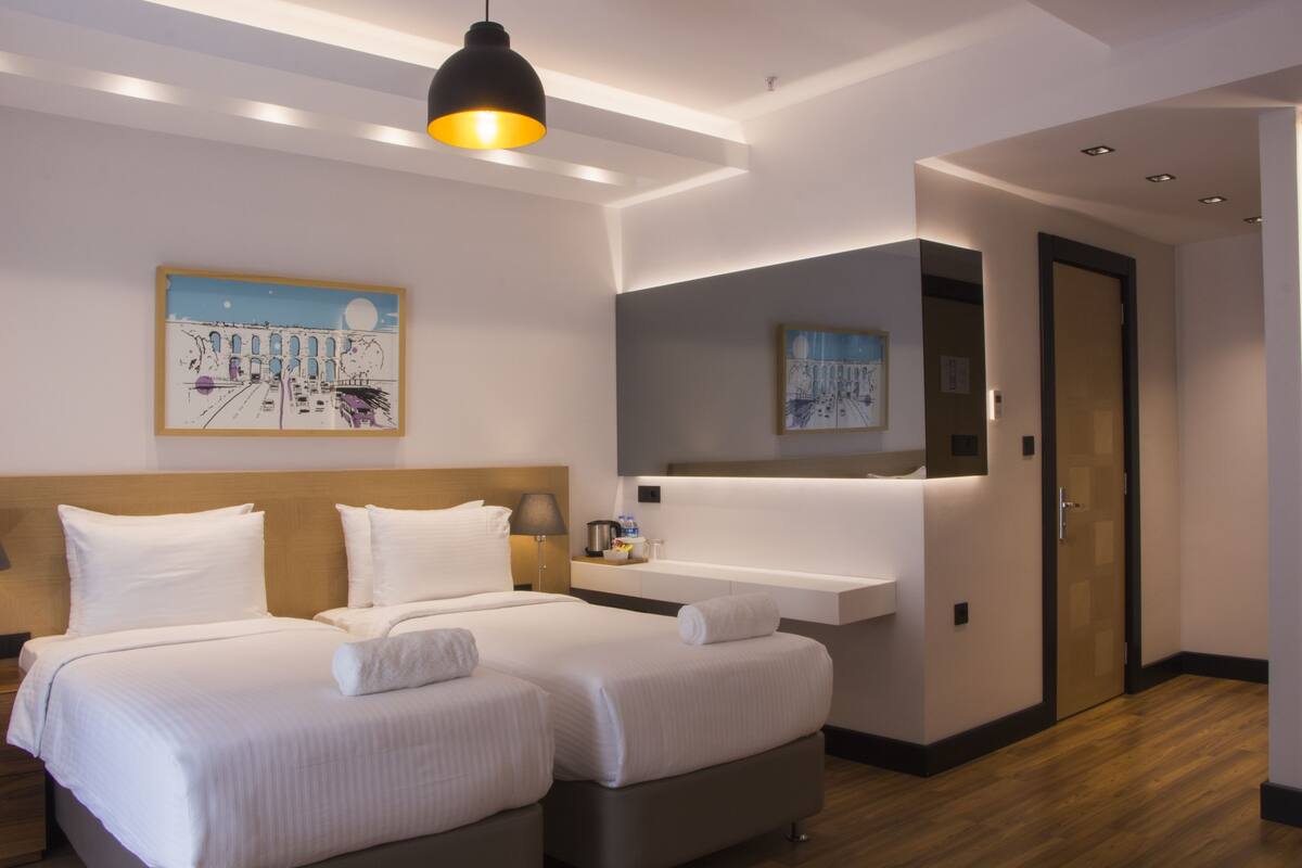 Una habitación de hotel moderna con una cama grande, mesitas de noche, un espejo y obras de arte en las paredes.
