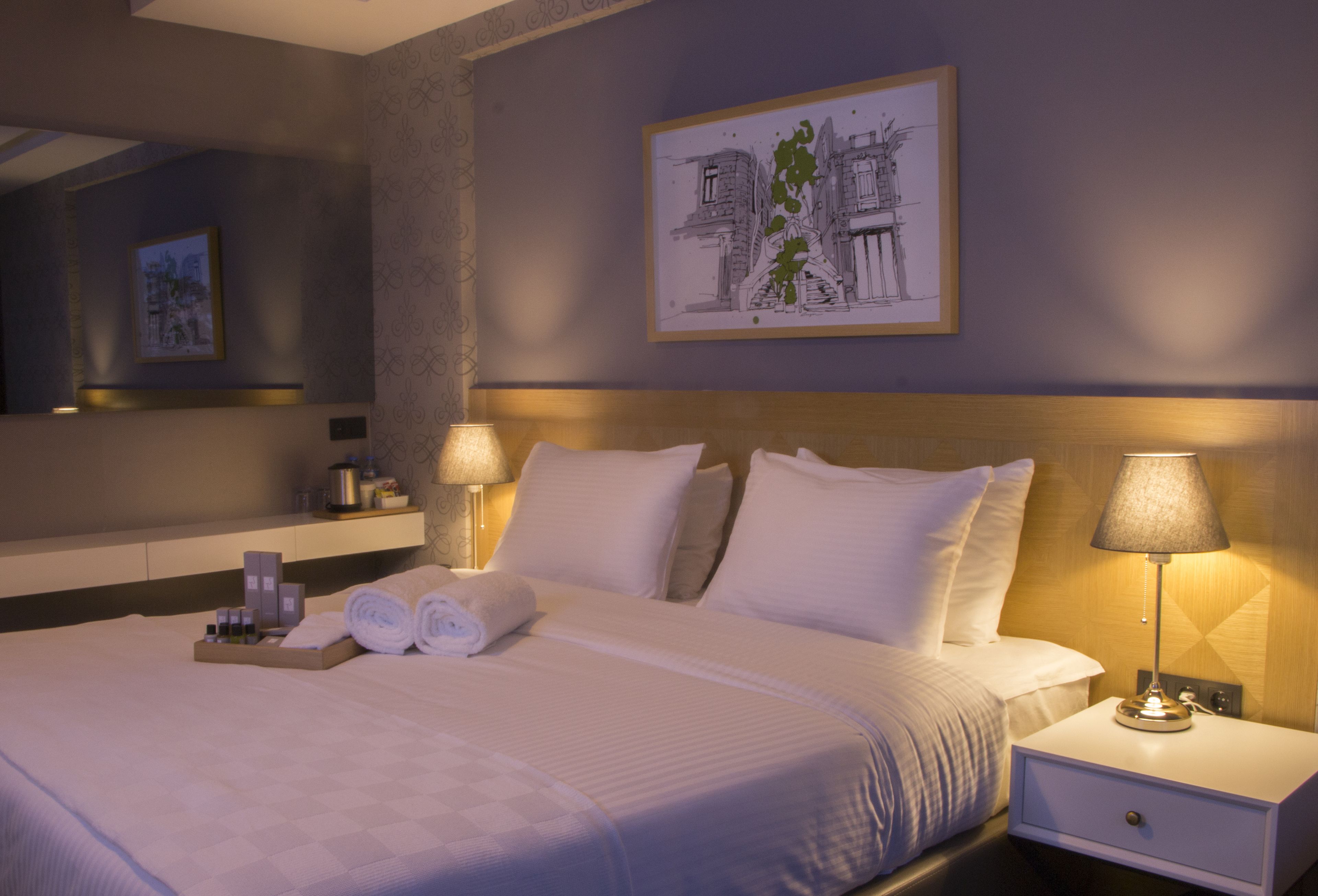 Un lit bien fait, avec du linge de lit blanc, une table de chevet avec une lampe et une œuvre d’art encadrée accrochée au mur.