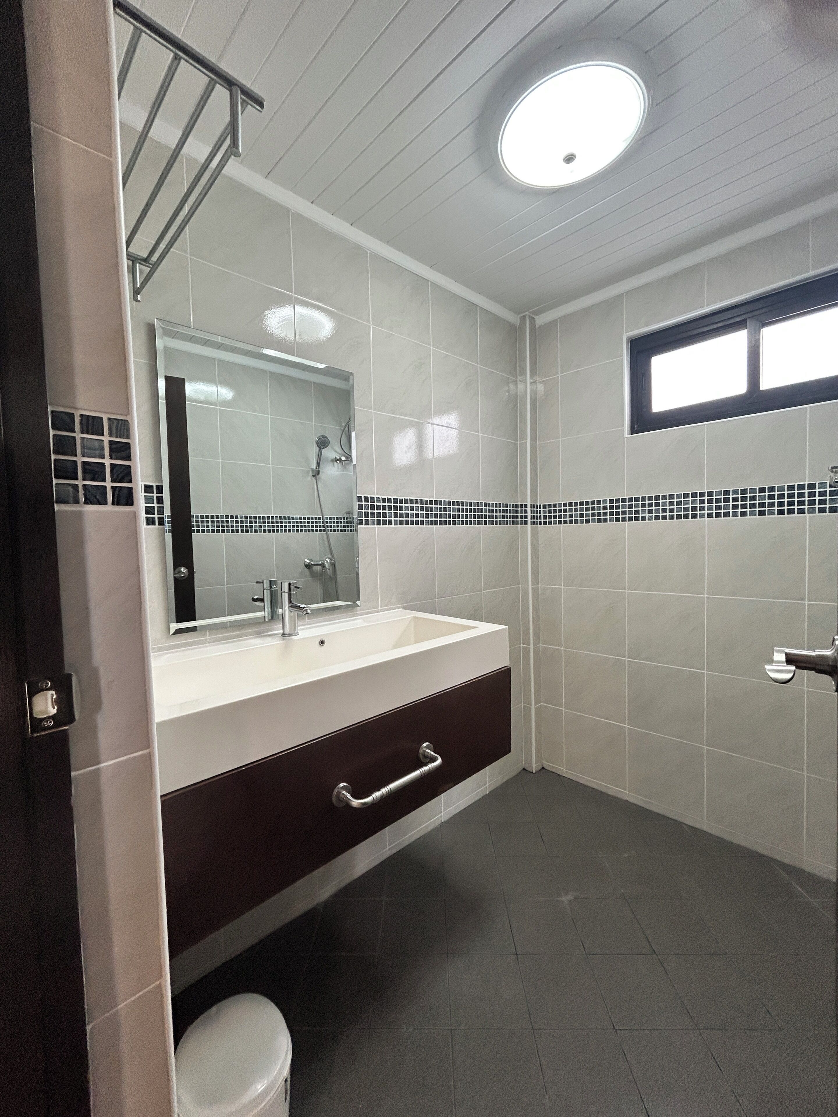 Ein Badezimmer mit weißem Waschbecken, dunklem Schrank, Spiegel und gefliesten Wänden.