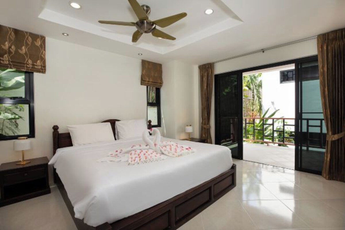 A hotel room with a bed, a ceiling fan, a nightstand, a window with a view, and a sliding glass door to the outside.