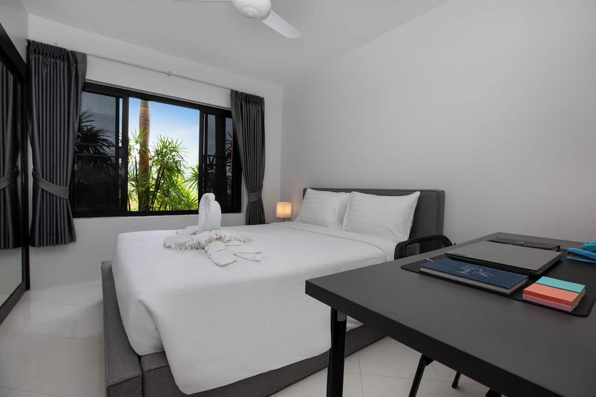 A modern hotel room with a large bed, a desk, and a view of palm trees through the window.