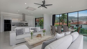 A modern living room with a sofa, coffee table, and dining area. - Baan Chom View Kamala (Kamala)
