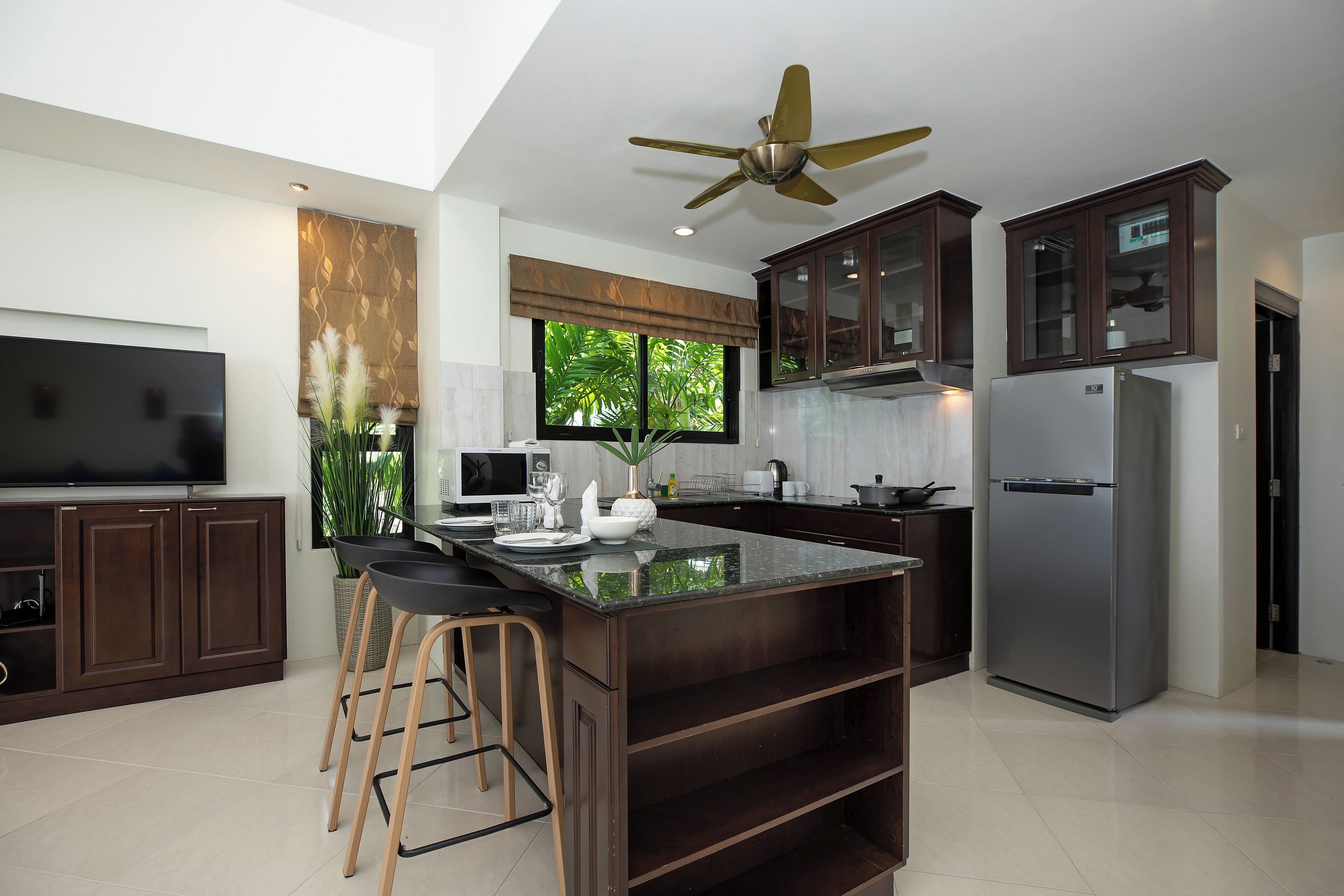 Una cocina moderna con armarios de madera oscura, una isla grande con taburetes, un ventilador de techo y un refrigerador empotrado.