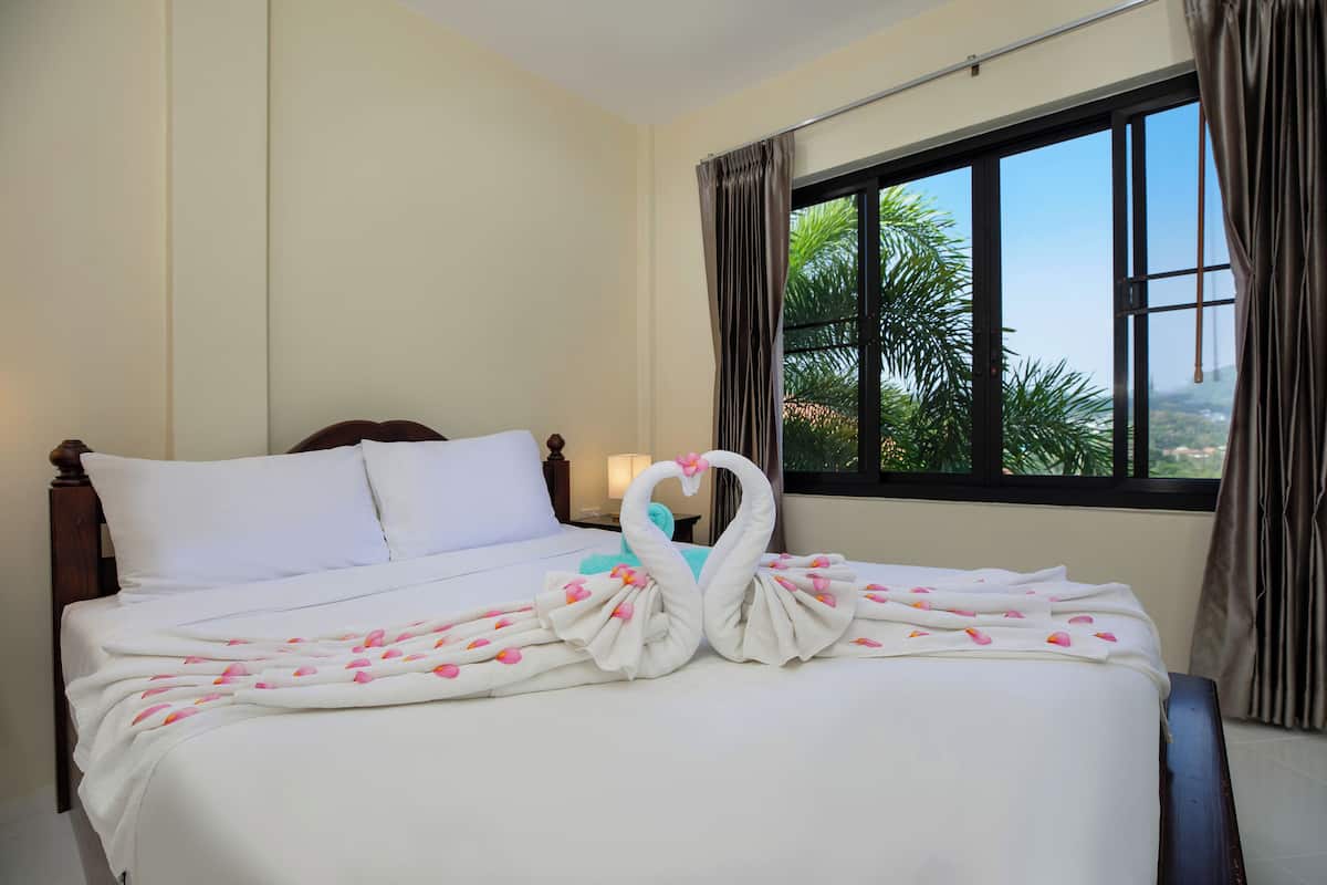 A hotel room with a bed, a window with curtains, and a view of palm trees.