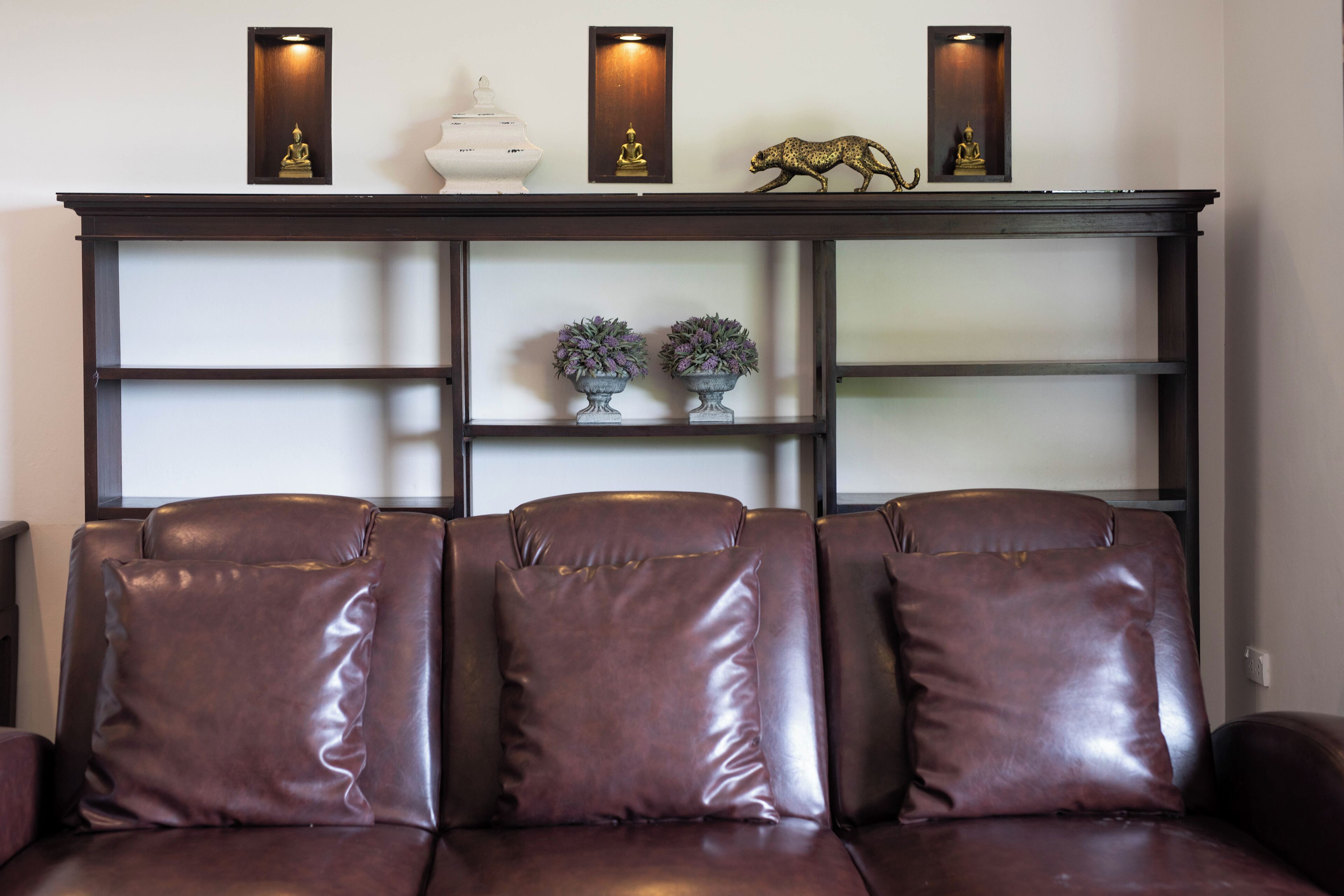 A brown leather sofa with a dark wooden console table above it, featuring decorative items and recessed lighting.