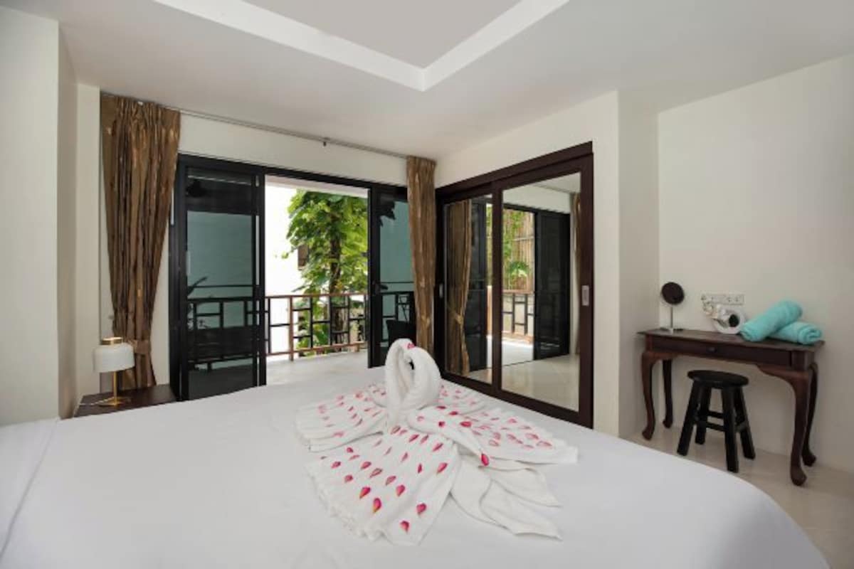 A hotel room with a bed, a desk, a chair, a lamp, and a view of the outdoors.