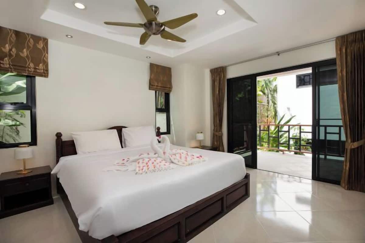 A hotel room with a bed, a ceiling fan, a nightstand, a window with a view, and a sliding glass door to the outside.