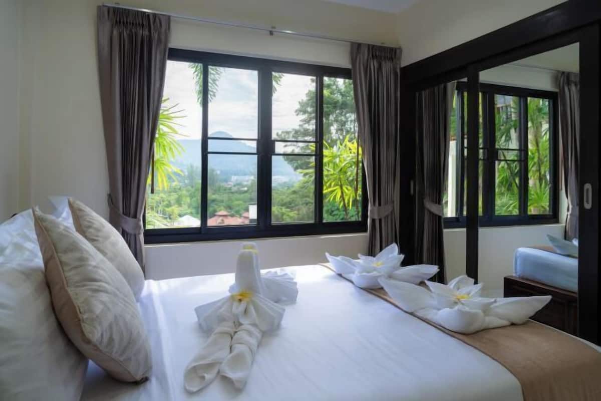 A hotel room with a bed, curtains, and a view of greenery.