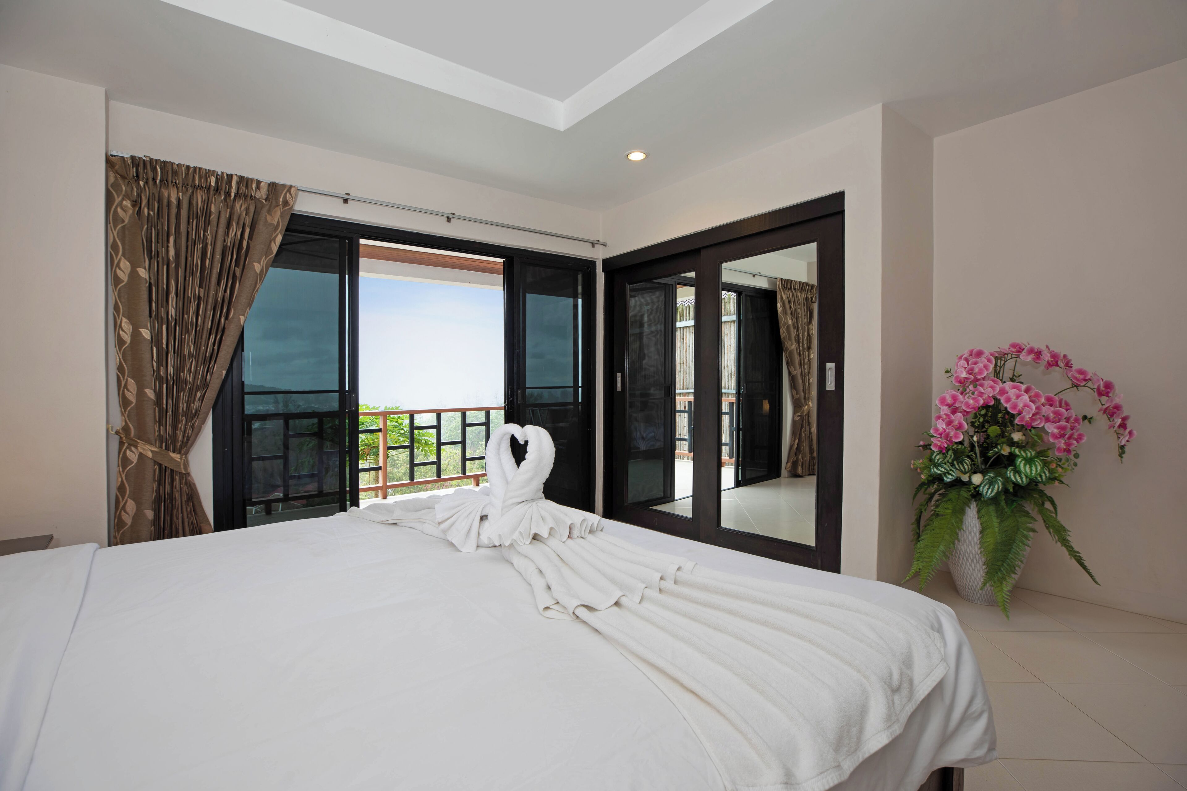 Habitación de hotel con una cama grande, un balcón con vistas y una planta en maceta.