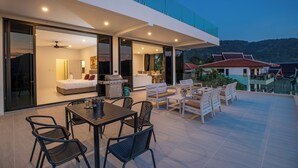 A modern house with a patio, a dining area, and a bedroom with a bed and a ceiling fan. - Baan Chom View Kamala (Kamala)