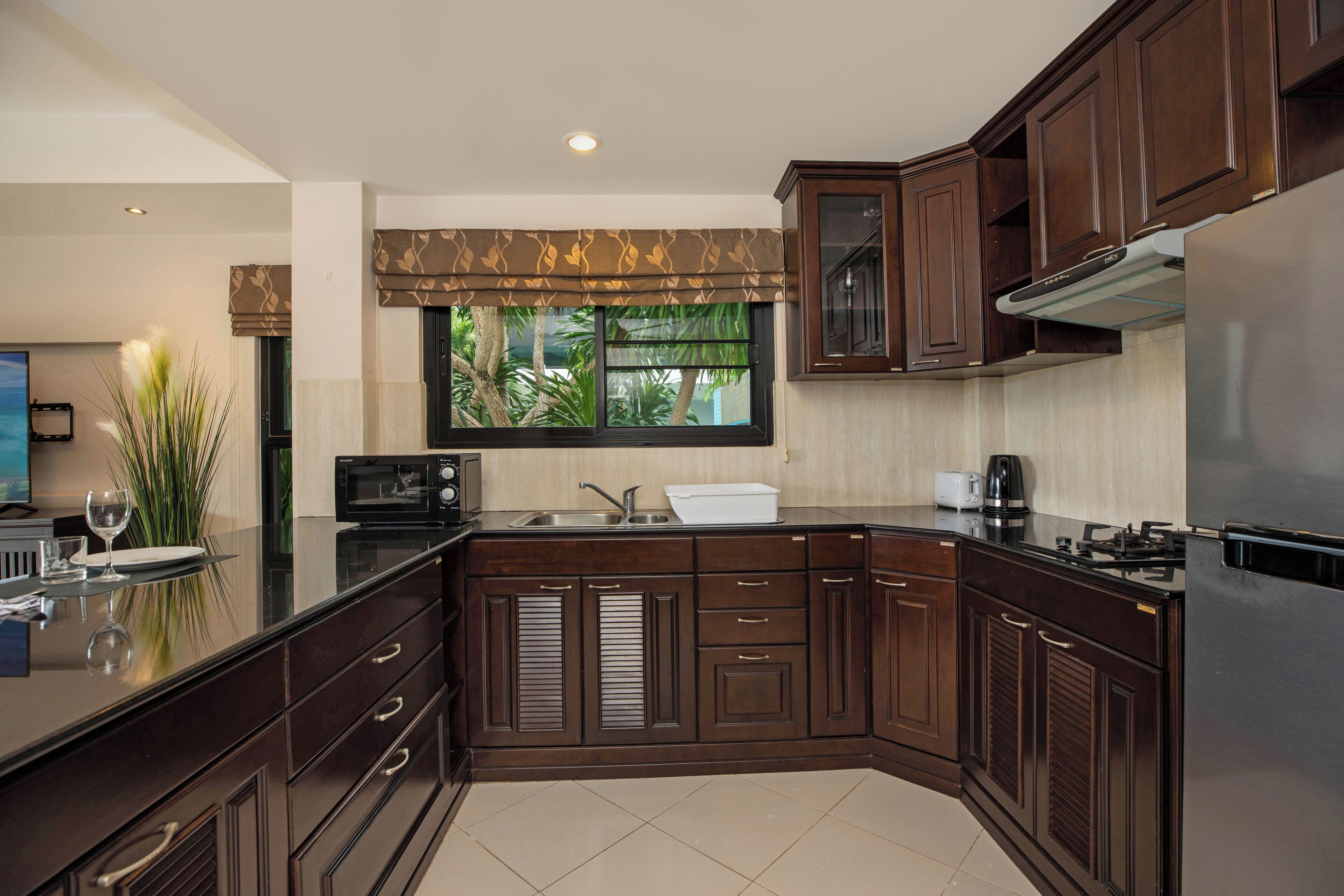 A modern kitchen with dark wood cabinets, a stainless steel refrigerator, and a large window with a view of greenery.