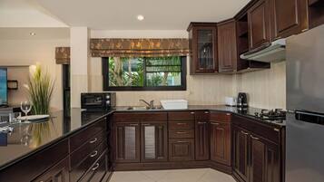 A modern kitchen with dark wood cabinets, a stainless steel refrigerator, and a large window with a view of greenery.