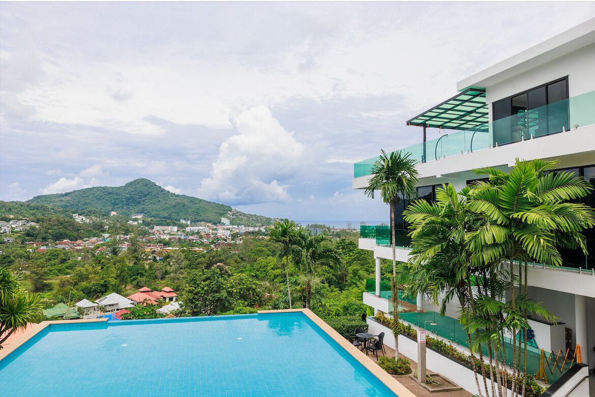 Un hotel moderno con piscina, vista su una montagna e vegetazione lussureggiante.