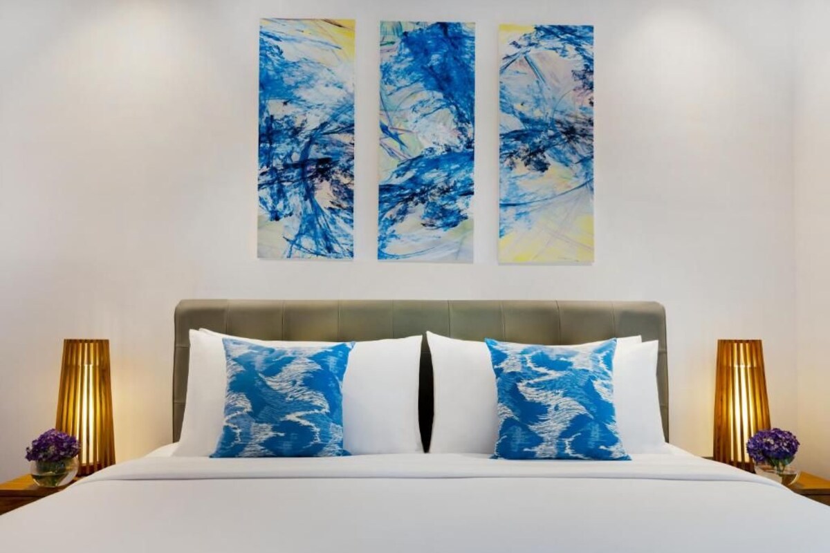 Una habitación de hotel con una cama, dos lámparas de noche y tres cuadros abstractos en la pared.