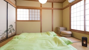 A traditional Japanese-style room with tatami flooring, a low bed with green bedding, a shoji screen, and a large window with a view. - Sano san chi (Izumisano)