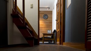 A hallway with wooden flooring, a staircase, and a bench with a clock on the wall. - Sano san chi (Izumisano)