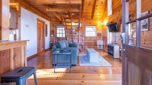 A wooden cabin interior with a sofa, a small table, a television, and a fireplace. - Sunrise Cabin- Hot Tub, WiFi, Firepit, Grill (Campton)