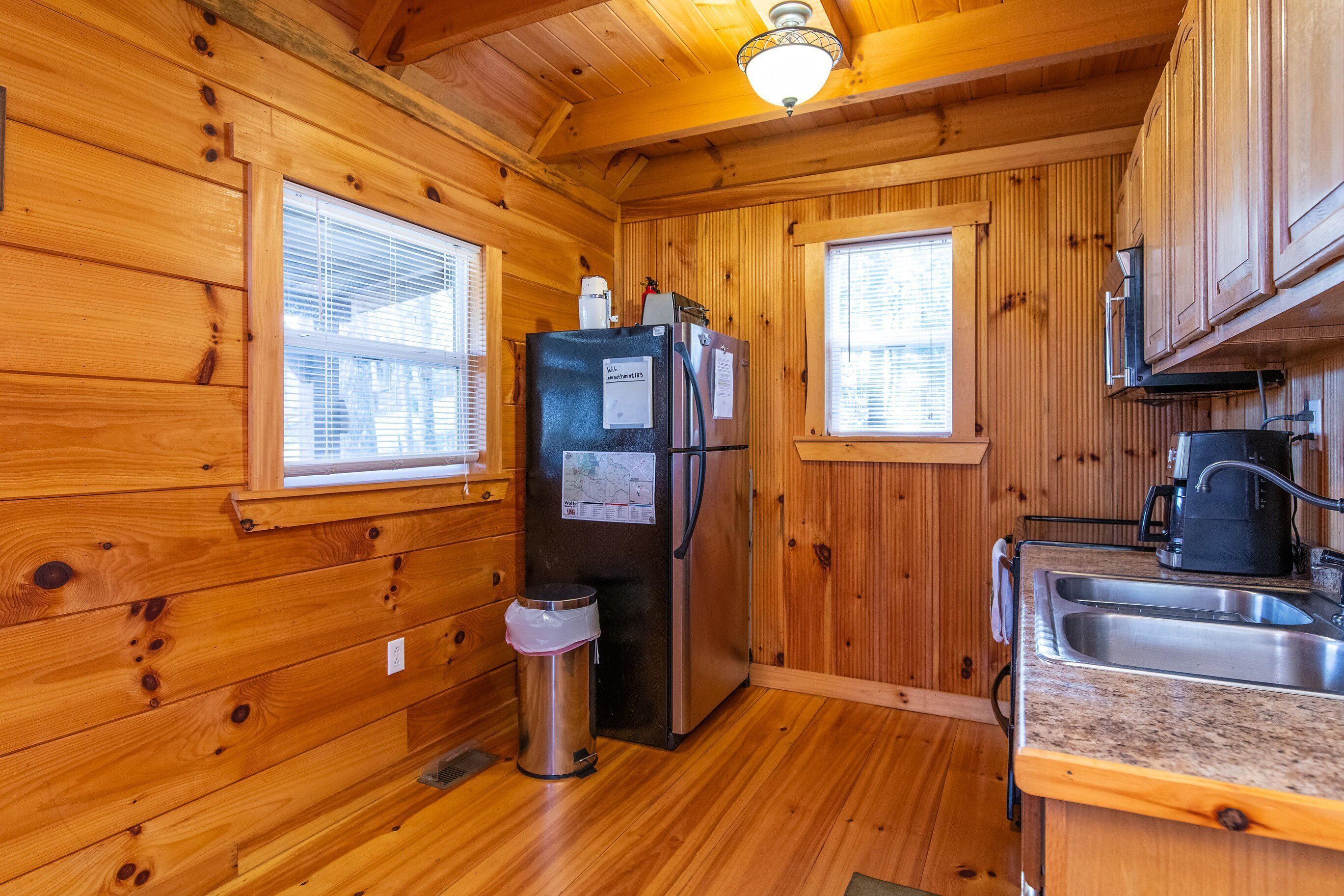 A wooden cabin kitchen with a refrigerator, sink, and a trash can.