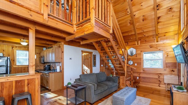 A wooden cabin interior with a kitchen, living area, and a staircase. - Sunrise Cabin- Hot Tub, WiFi, Firepit, Grill (Campton)