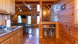 A wooden cabin interior with a kitchen, dining area, and a living room. - Sunrise Cabin- Hot Tub, WiFi, Firepit, Grill (Campton)