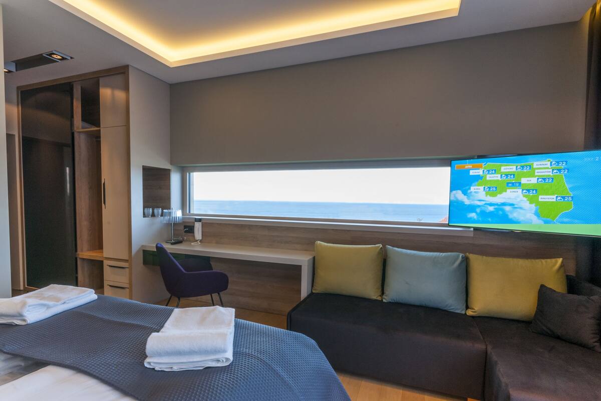 Une chambre d’hôtel moderne équipée d’un lit, d’un bureau et d’un téléviseur affichant une carte météorologique.