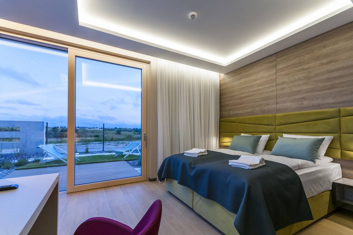 Une chambre d’hôtel moderne, dotée d’un grand lit, d’un bureau, d’une chaise et offrant une vue sur l’extérieur.