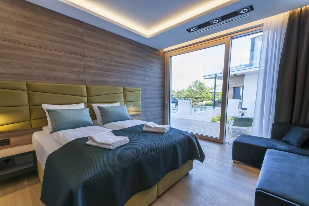 Une chambre d’hôtel moderne, dotée d’un grand lit, d’un canapé et d’une porte-fenêtre coulissante donnant sur un balcon.