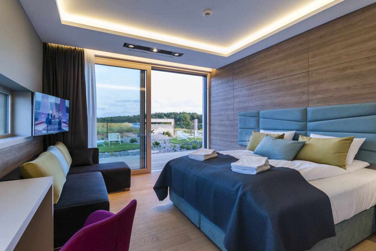 Une chambre d’hôtel moderne dotée d’un grand lit, d’un canapé, d’une télévision et d’une porte-fenêtre coulissante donnant sur un espace extérieur.