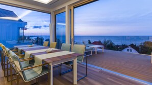 A modern outdoor dining area with a view of the sea, featuring a wooden deck, metal-framed tables, and cushioned chairs. - Przystan Mechelinki - Marina del Mar (Kosakowo)