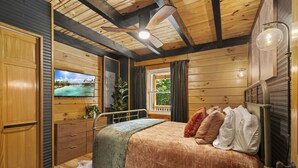 A cozy wooden cabin bedroom with a bed, a TV, and a view of the outdoors.