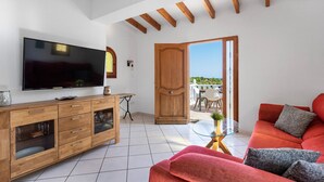 Uma sala de estar com televisão, móveis de madeira, mesa de centro de vidro e um sofá vermelho.