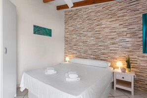 Een hotelkamer met een bed, twee nachtkastjes, een muur met een structuur, een schilderij en een potplant.
