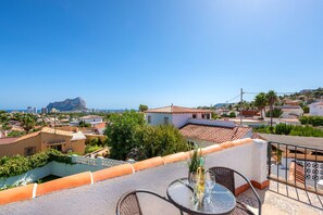 A rooftop terrace with a table and chairs, overlooking a coastal town with buildings and a mountain in the distance.