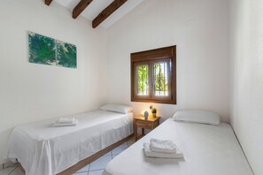A room with two single beds, a small bedside table with a lamp, and a window with bars.