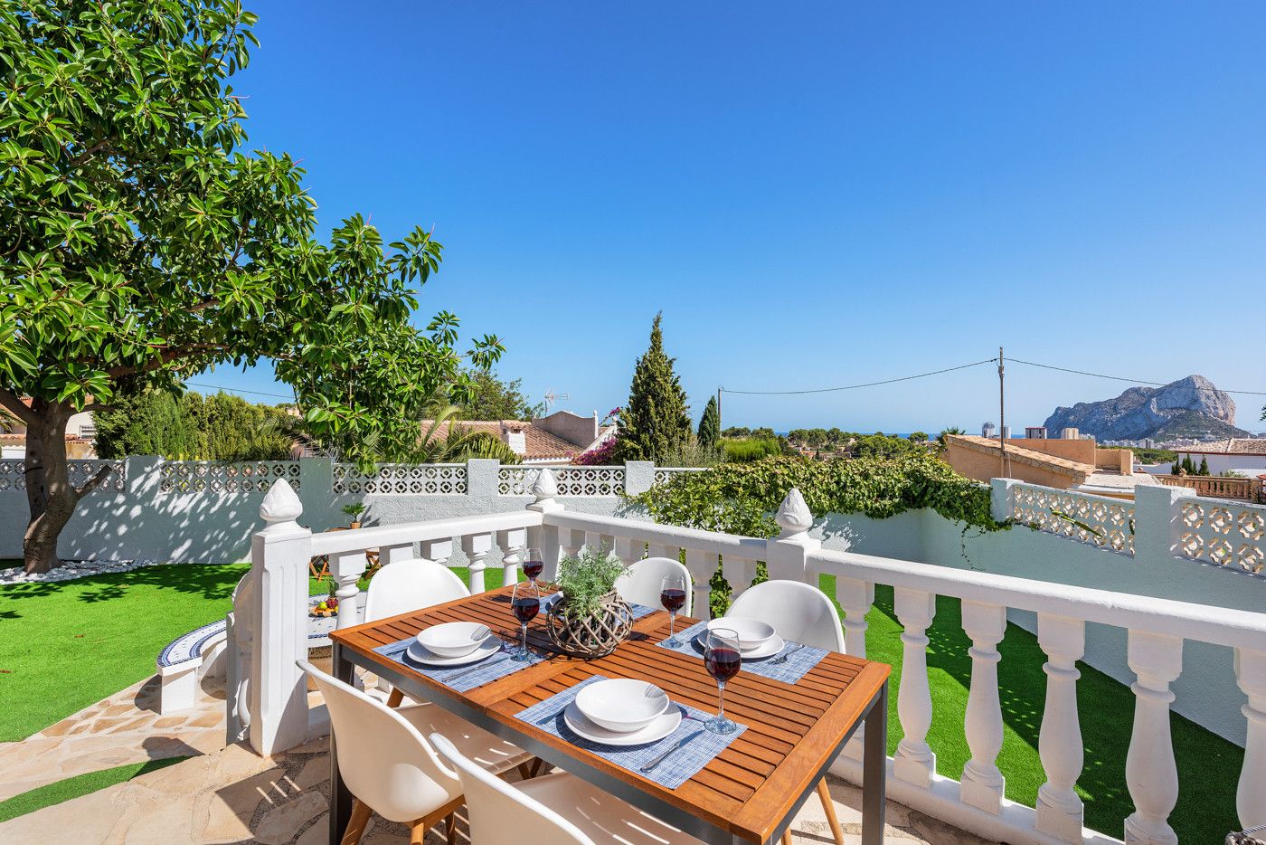 En terrasse med et bord dækket til to, med udsigt over en have og et bjerglandskab.