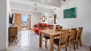 Uma sala ampla com uma mesa de jantar, cadeiras de madeira e um sofá vermelho. Há uma varanda com vista para a cidade.