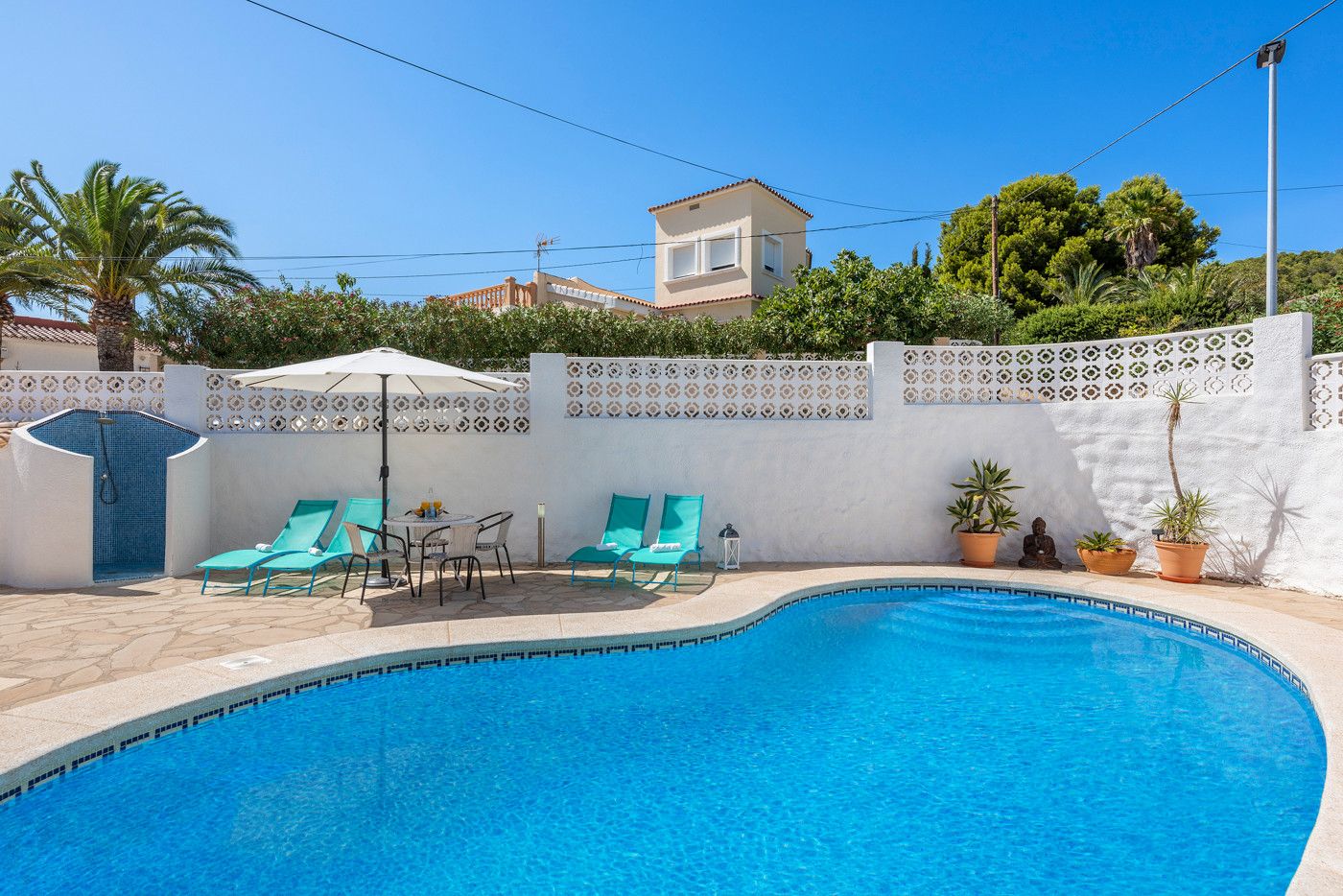 A swimming pool with a tiled deck, surrounded by a white wall with decorative patterns, and a small patio area with a table and chairs.