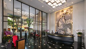 Un hall de hotel con mostrador de recepción, zona de estar y grandes ventanales con vistas a la calle.