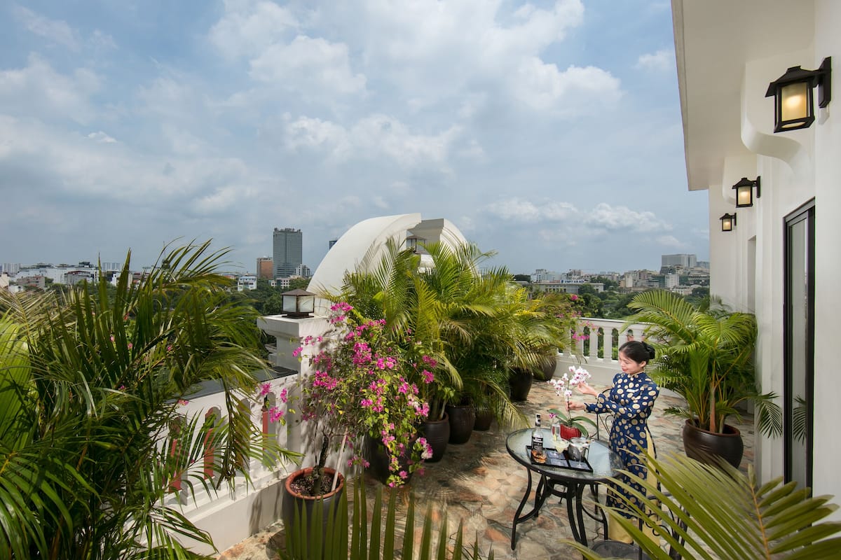 Una terraza en la azotea con plantas en macetas, una mesa y una persona cuidando flores.