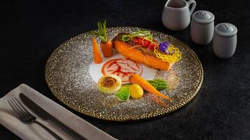 A plate of food with vegetables and a decorative garnish, accompanied by a napkin and cutlery on a dark surface.