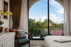Een hotelkamer met een groot raam, een bed, een stoel, een tafel met een schaal fruit en een kamerplant.